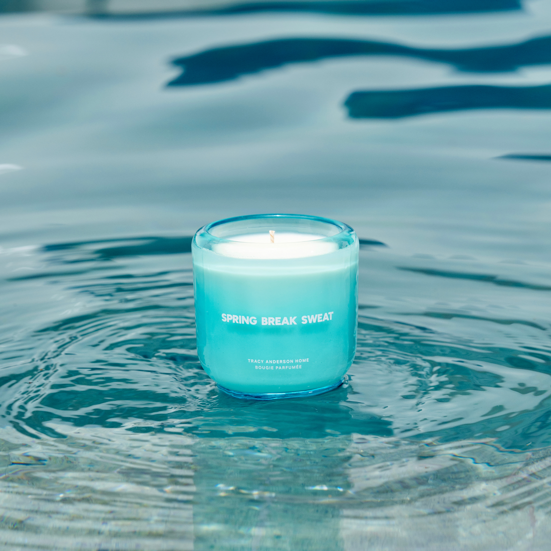 The Tracy Anderson Spring Break Sweat candle resting in a shimmering pool of water.